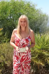 Imagem de Cláudia Machado de Castro, especialista em Feng Shui em Portugal, sorridente ao sol segurando um bússola Feng Shui, destacando seu trabalho na harmonização de ambientes. Psicóloga e consultora com experiência em equilibrar energias para melhorar qualidade de vida.